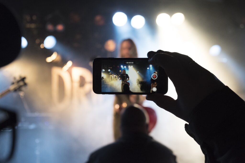 Une personne filmant un évènement sur scène avec son smartphone.